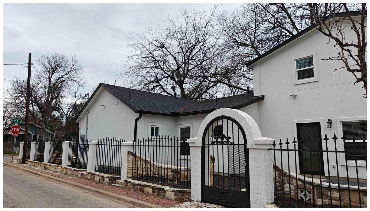 Unique corner view of Zeta House's white stucco exterior, featuring castle-like iron fences and gates, illustrating the architectural style of the property